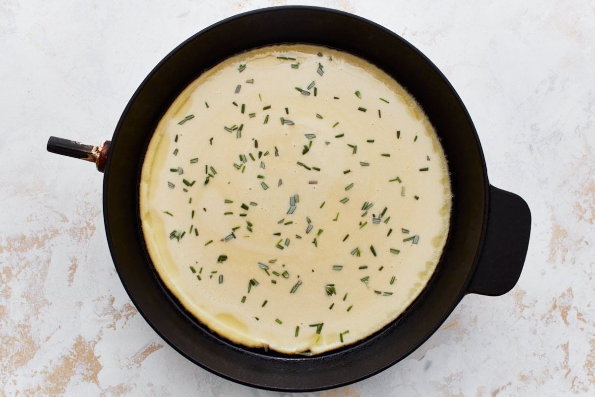 Uncooked chickpea batter in a skillet, sprinkled with chopped rosemary.