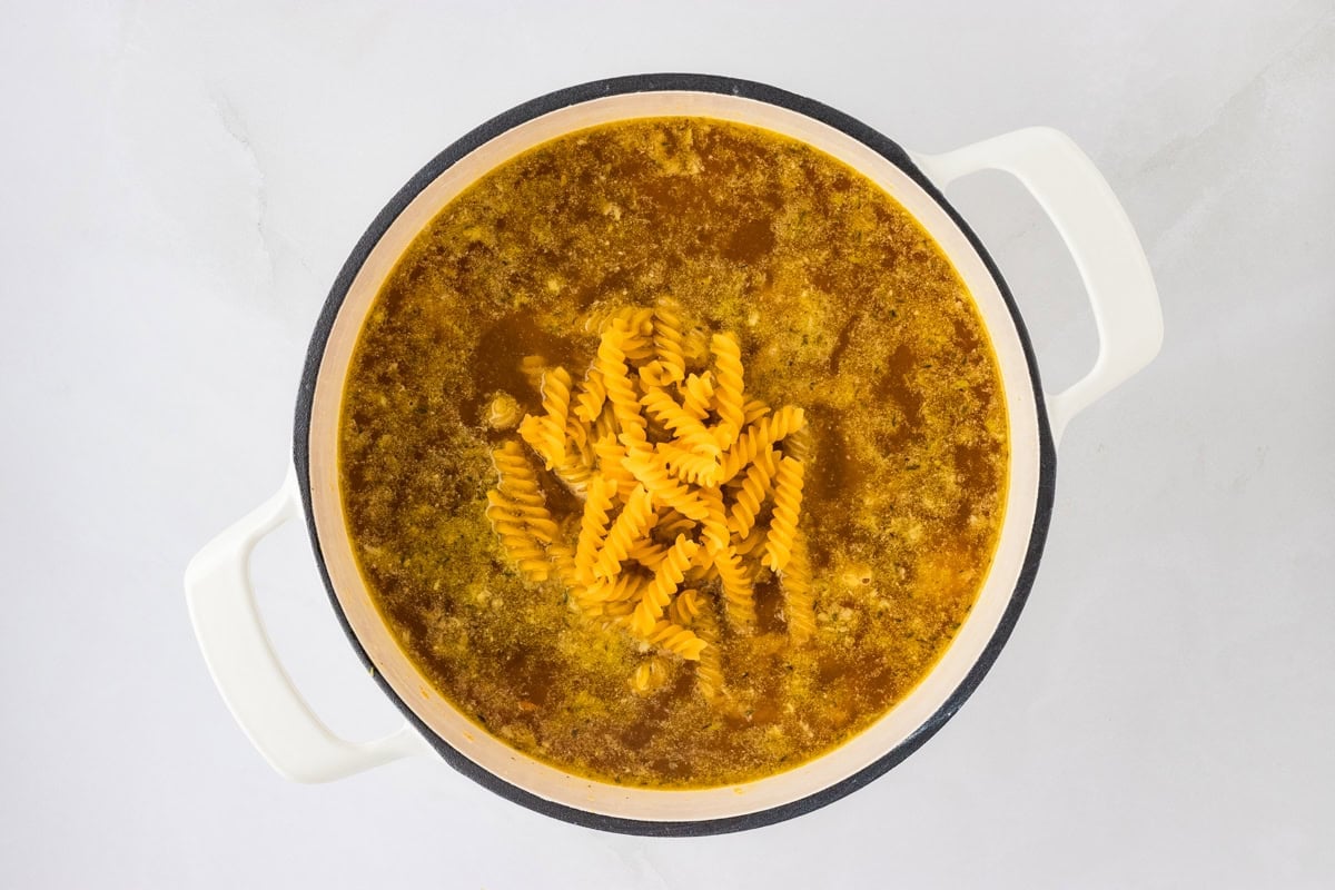 A pot of gluten-free spiral noodles added into the chicken broth, showcasing the cooking process.