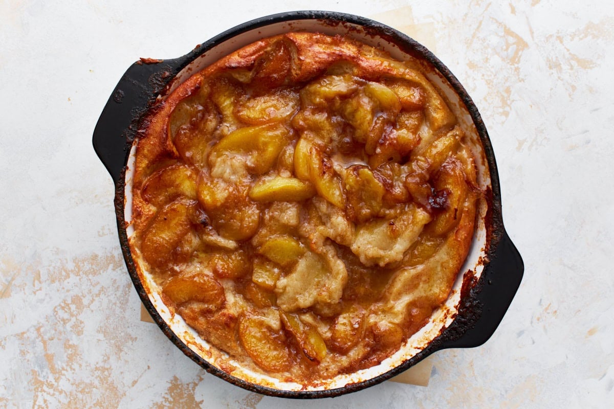 A close-up of a golden brown peach cobbler baked in a black skillet, showing caramelized edges and bubbling peach filling.