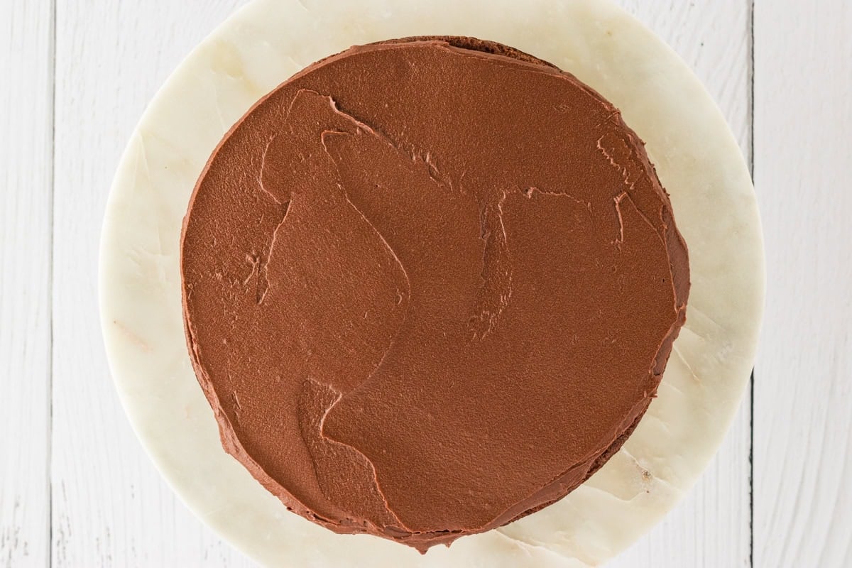 The first cake layer covered with a smooth layer of chocolate frosting, evenly spread over the top.