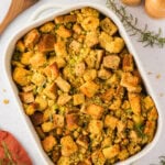A baked dish of golden-brown gluten-free cornbread stuffing with herbs, served in a white casserole dish with a wooden spoon and fresh rosemary nearby.