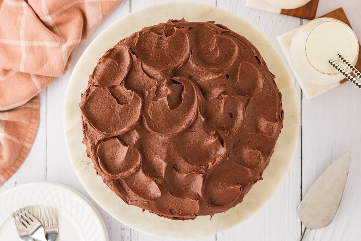 A fully frosted gluten-free chocolate cake with swirls of rich chocolate frosting on top, placed on a marble cake stand.