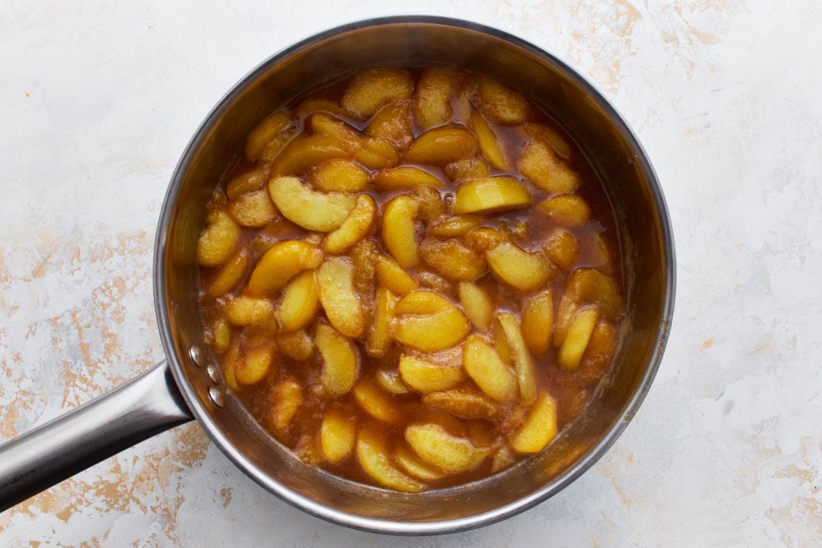 A saucepan filled with freshly cooked peach filling, featuring golden peach slices coated in a rich, syrupy sauce.