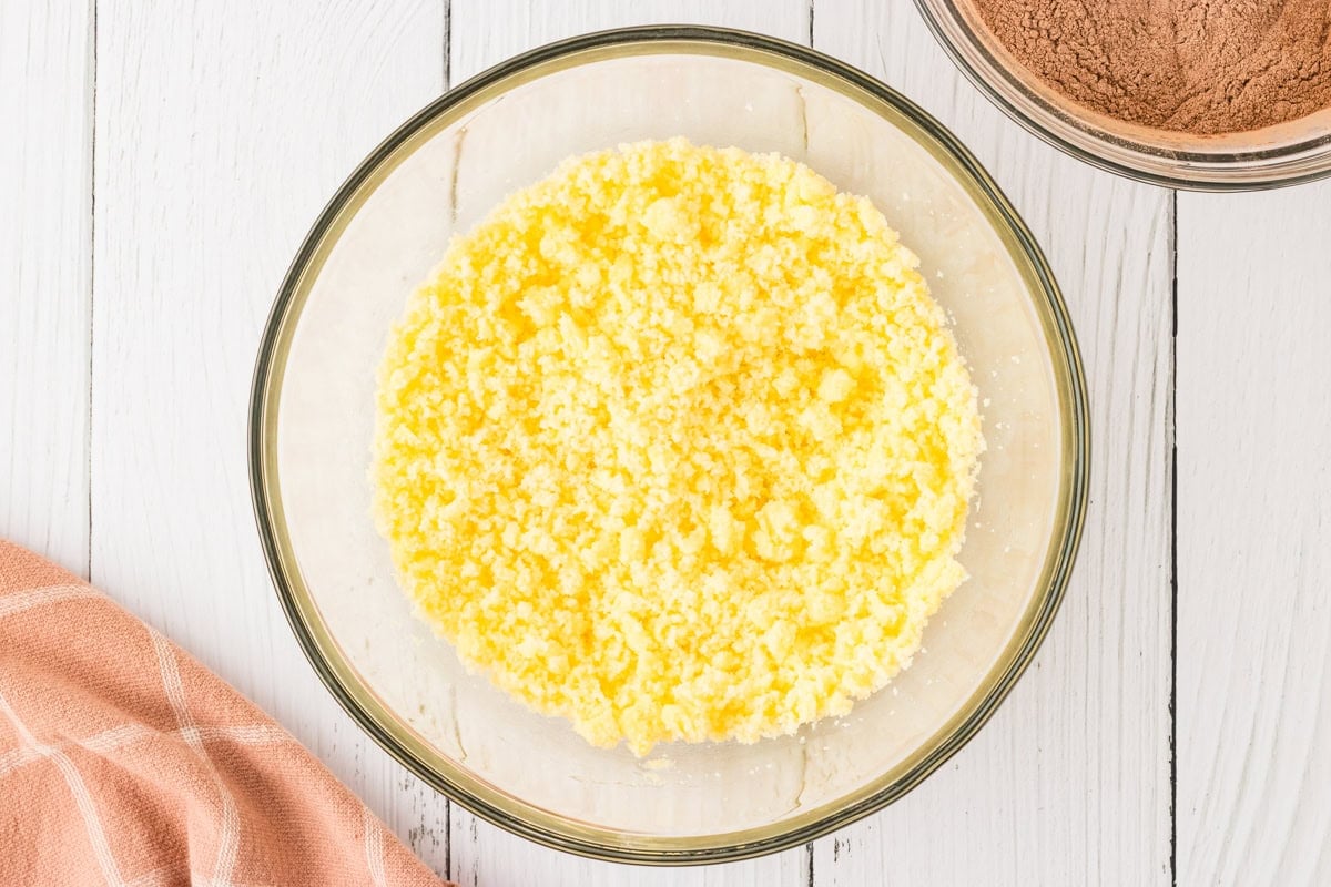 A glass mixing bowl with softened butter and sugar, creamed together, placed on a white wooden surface.