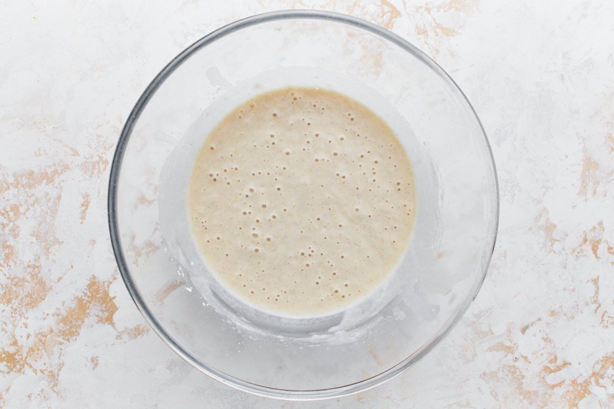 A glass mixing bowl filled with frothy gluten-free cobbler batter, ready to be poured into the baking dish.