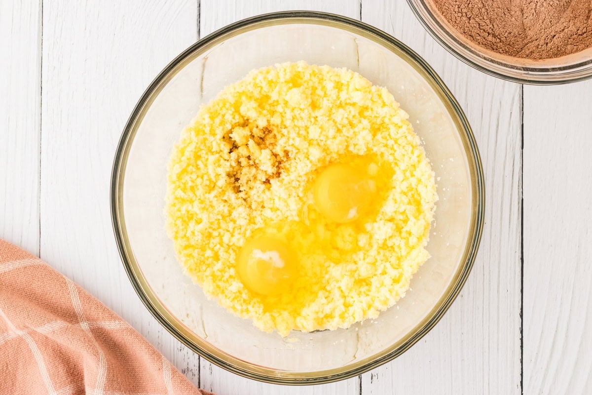 The same butter and sugar mixture now with two cracked eggs and vanilla extract added on top, ready for mixing.