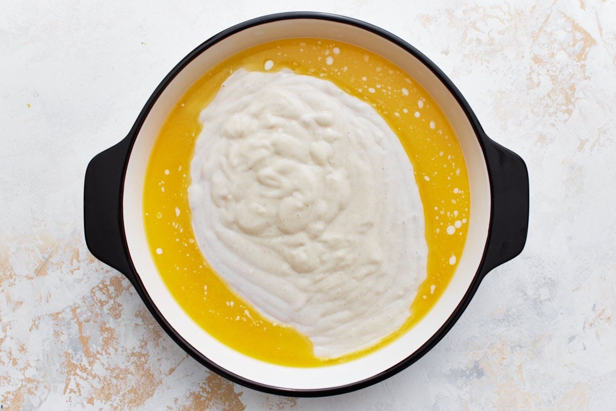 A baking dish with cobbler gluten-free batter poured over melted butter, showing the smooth and creamy batter surface.