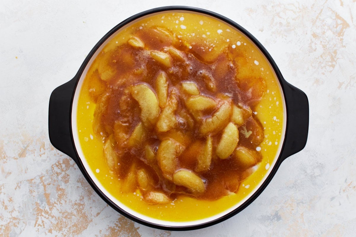 A round baking dish with peach filling placed on top of a layer of cobbler batter and melted butter, ready to be baked.