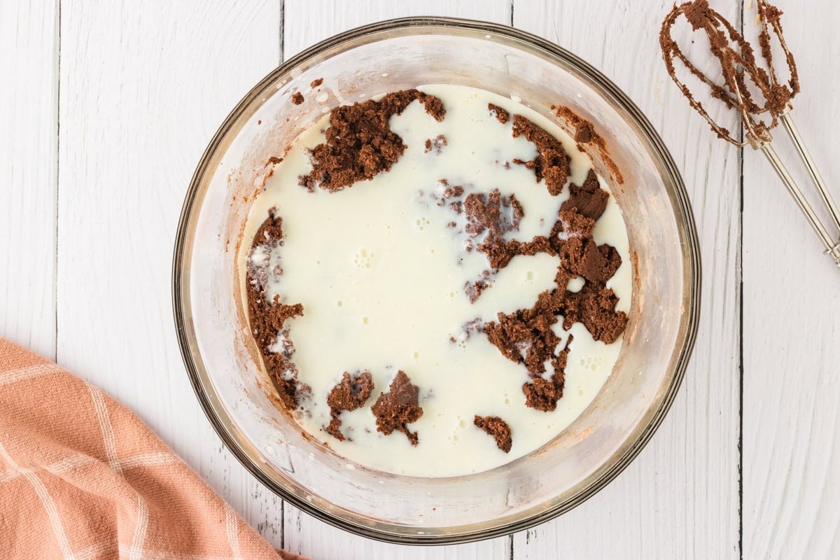 The chocolate cake batter partially mixed, with buttermilkl just added, showing an uneven mixture of dry and wet ingredients.