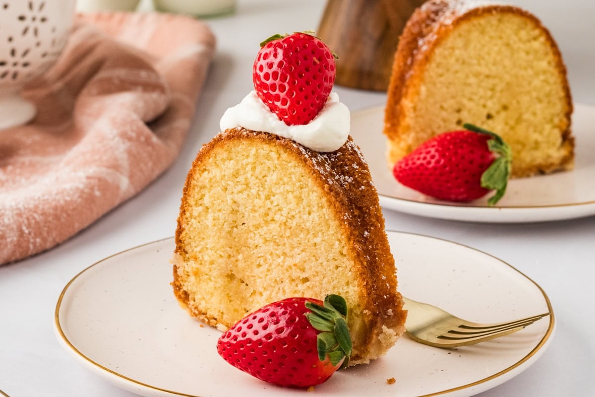 Slice of gluten-free Kentucky butter cake topped with whipped cream and a fresh strawberry on a white plate, showing the moist crumb and golden glaze.