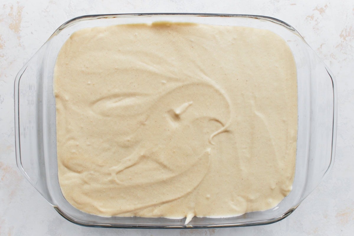 A baking dish with the second layer of cake batter spread over the cinnamon sugar filling, creating a smooth top.