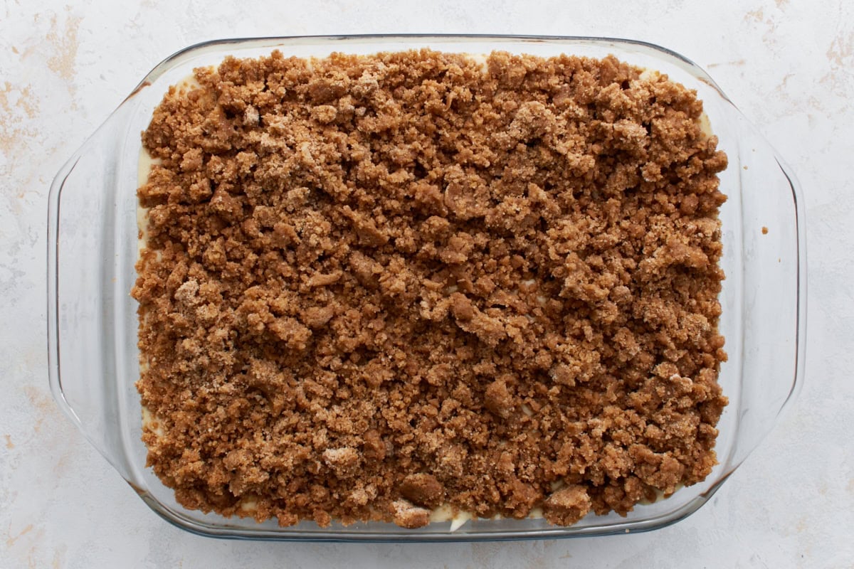A glass baking dish filled with gluten-free coffee cake batter, generously topped with a thick layer of cinnamon-sugar streusel before baking.