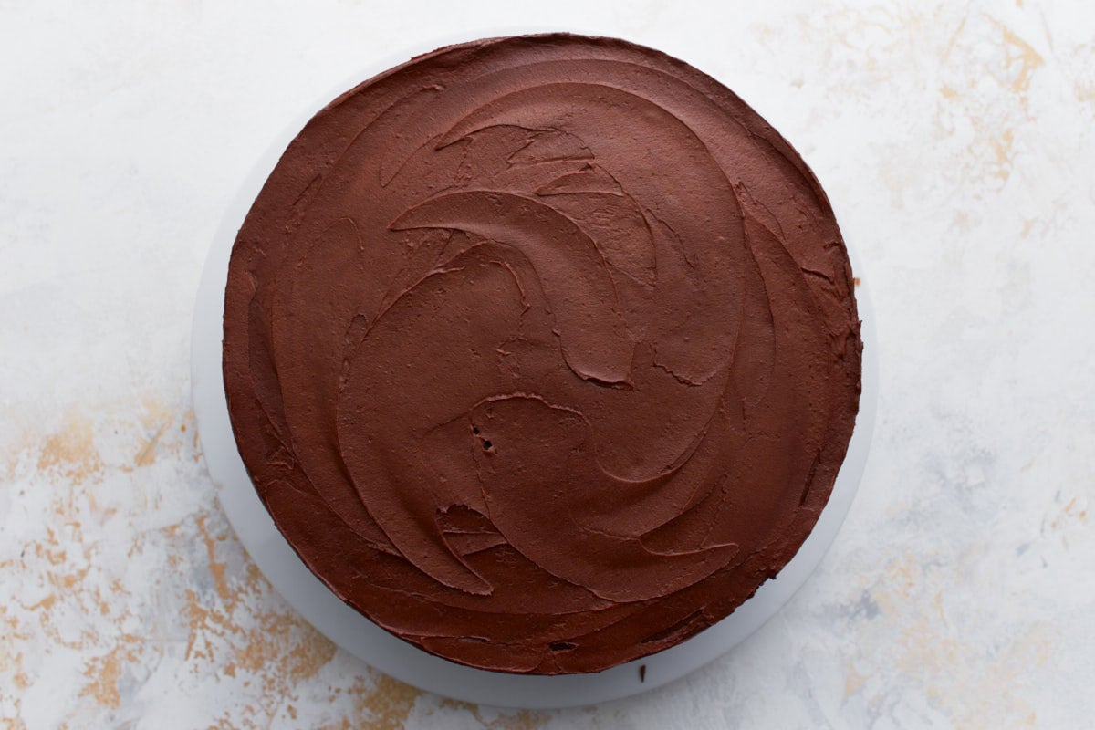 A gluten-free birthday cake completely covered in smooth chocolate buttercream with elegant swirl patterns.