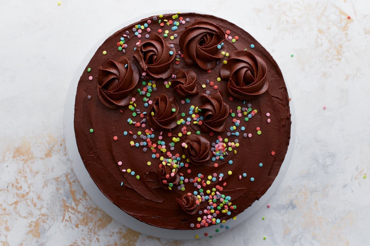 A fully decorated gluten-free cake with chocolate buttercream swirls and colorful sprinkles scattered across the top.