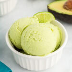 A close-up of two scoops of creamy avocado ice cream in a white ramekin, garnished with a fresh lime wedge.