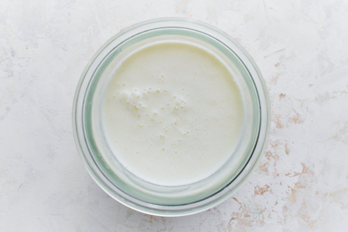 A glass bowl filled with homemade buttermilk, a mixture of milk and vinegar, showing a slightly curdled texture.