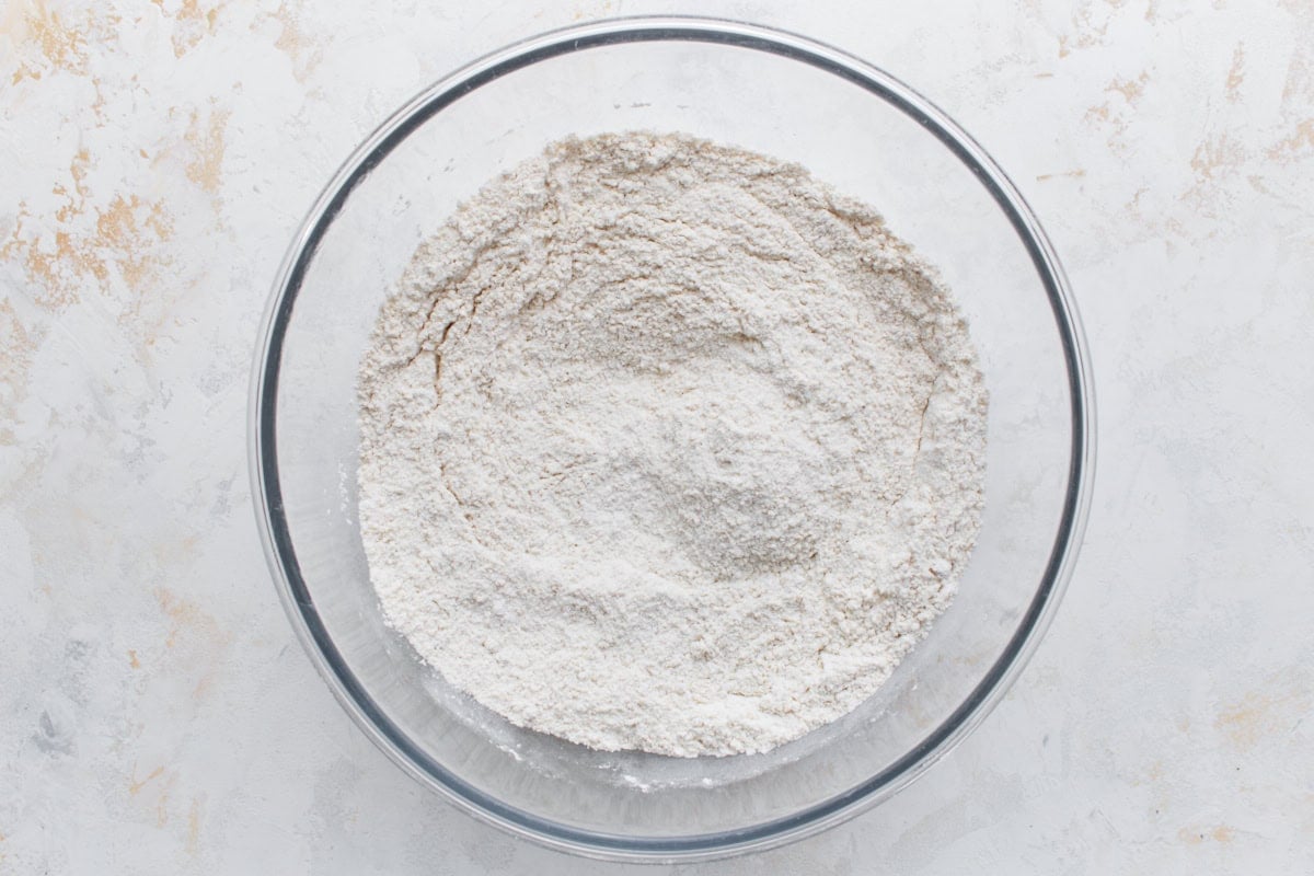 A glass mixing bowl containing a blend of gluten-free flour, baking powder, and sugar, evenly mixed and ready for baking.