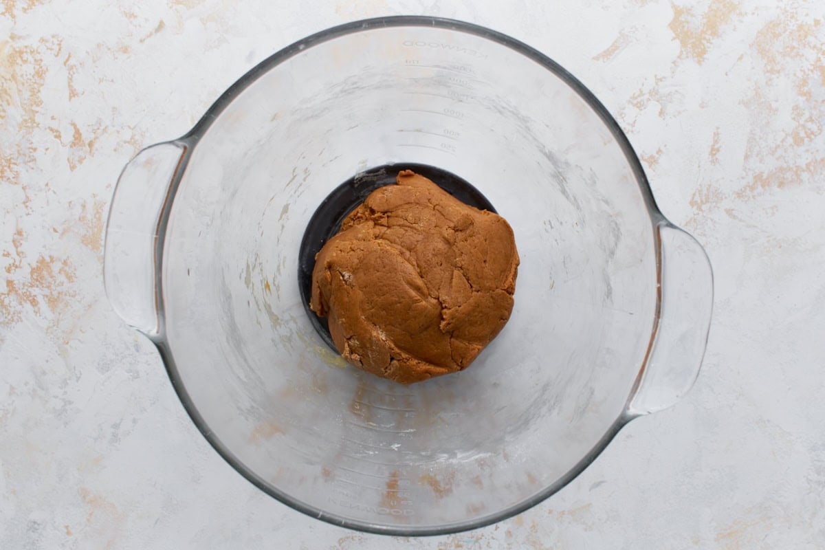 A glass mixing bowl with a ball of dough for gluten-free graham crackers. The dough is smooth, brown, and well-formed.