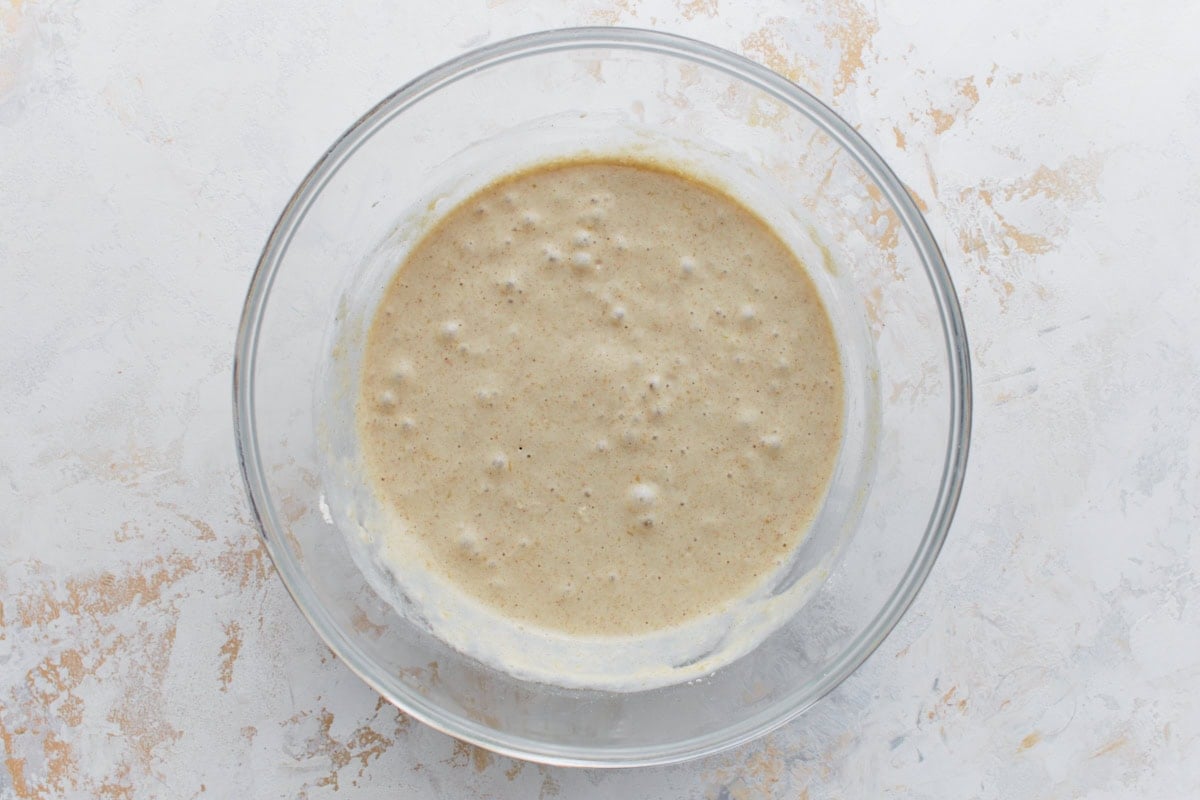 A bowl of pancake batter with small bubbles forming on the surface, indicating that the ingredients have been mixed and are reacting, ready for cooking.