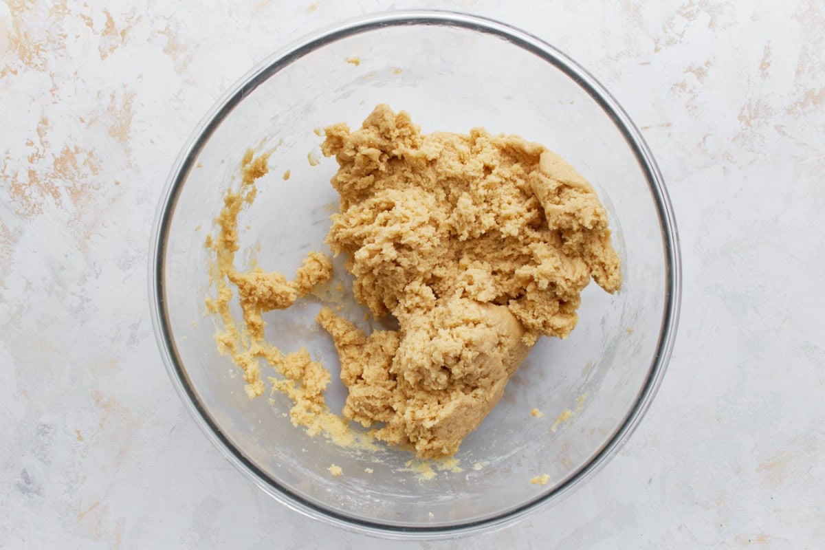 A bowl of gluten-free cake batter in its early stages, appearing thick and crumbly before additional liquids are added.