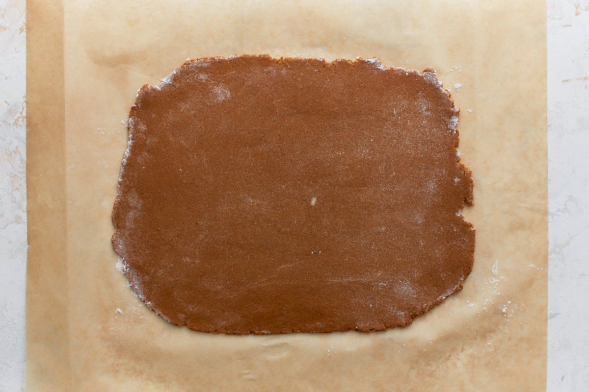 Rolled-out gluten-free graham cracker dough on parchment paper. The dough is evenly spread and lightly dusted with flour.