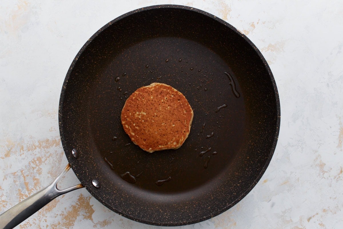 A fully cooked buckwheat pancake flipped to its golden-brown side, sitting in a non-stick pan with a bit of oil residue, ready to be plated.