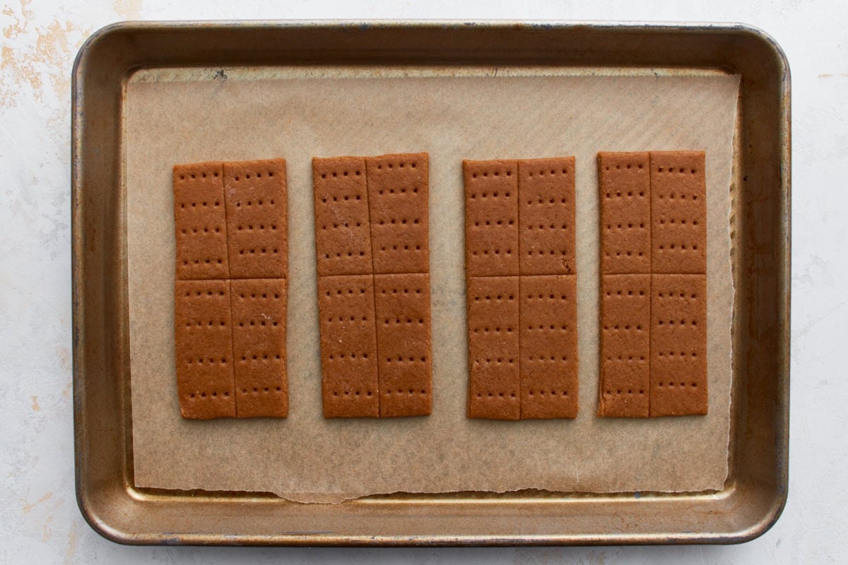 A baking sheet with gluten-free graham cracker dough that has been scored into smaller rectangles and pierced with a fork for the classic cracker pattern.