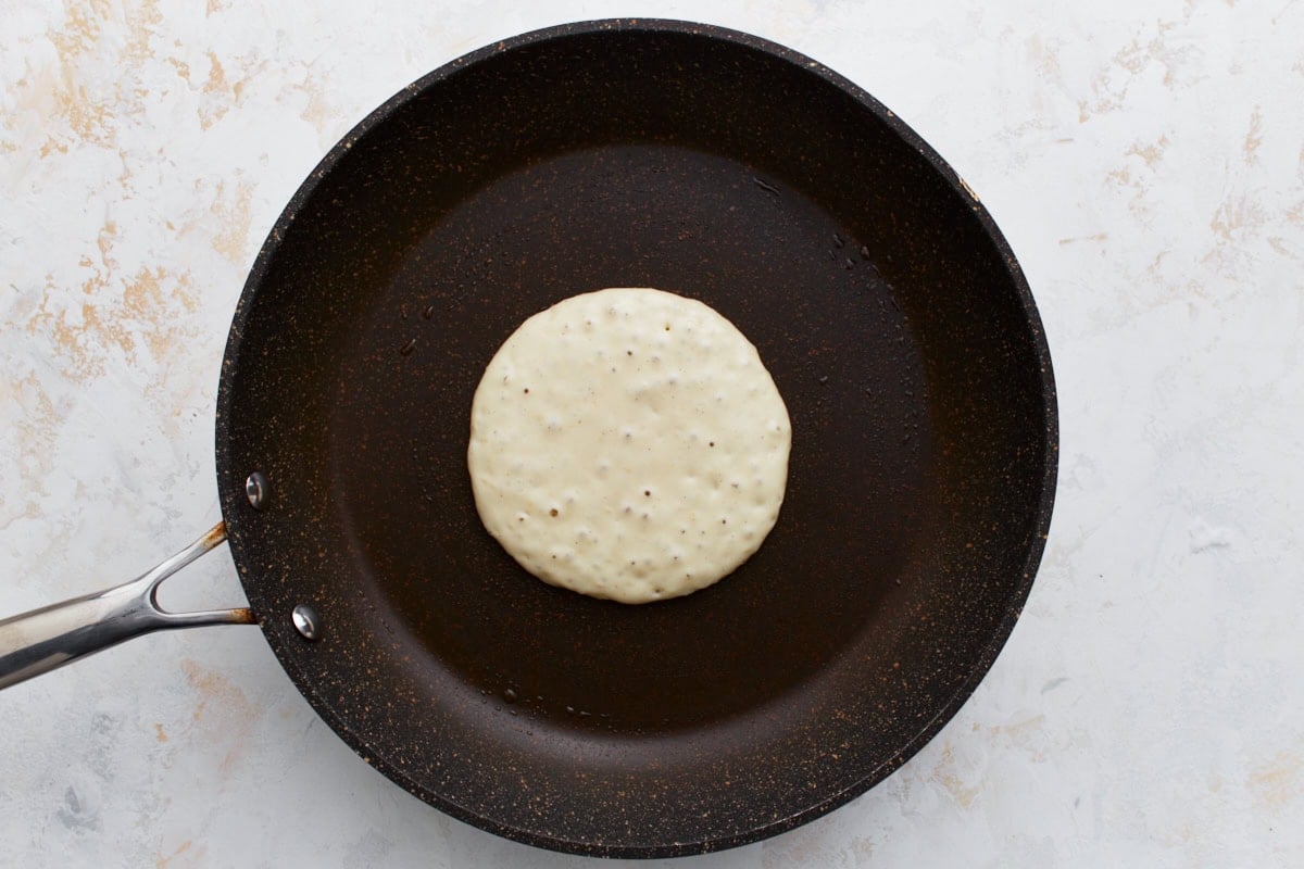 A pancake on the skillet showing small bubbles forming on the surface, indicating it’s ready to flip.
