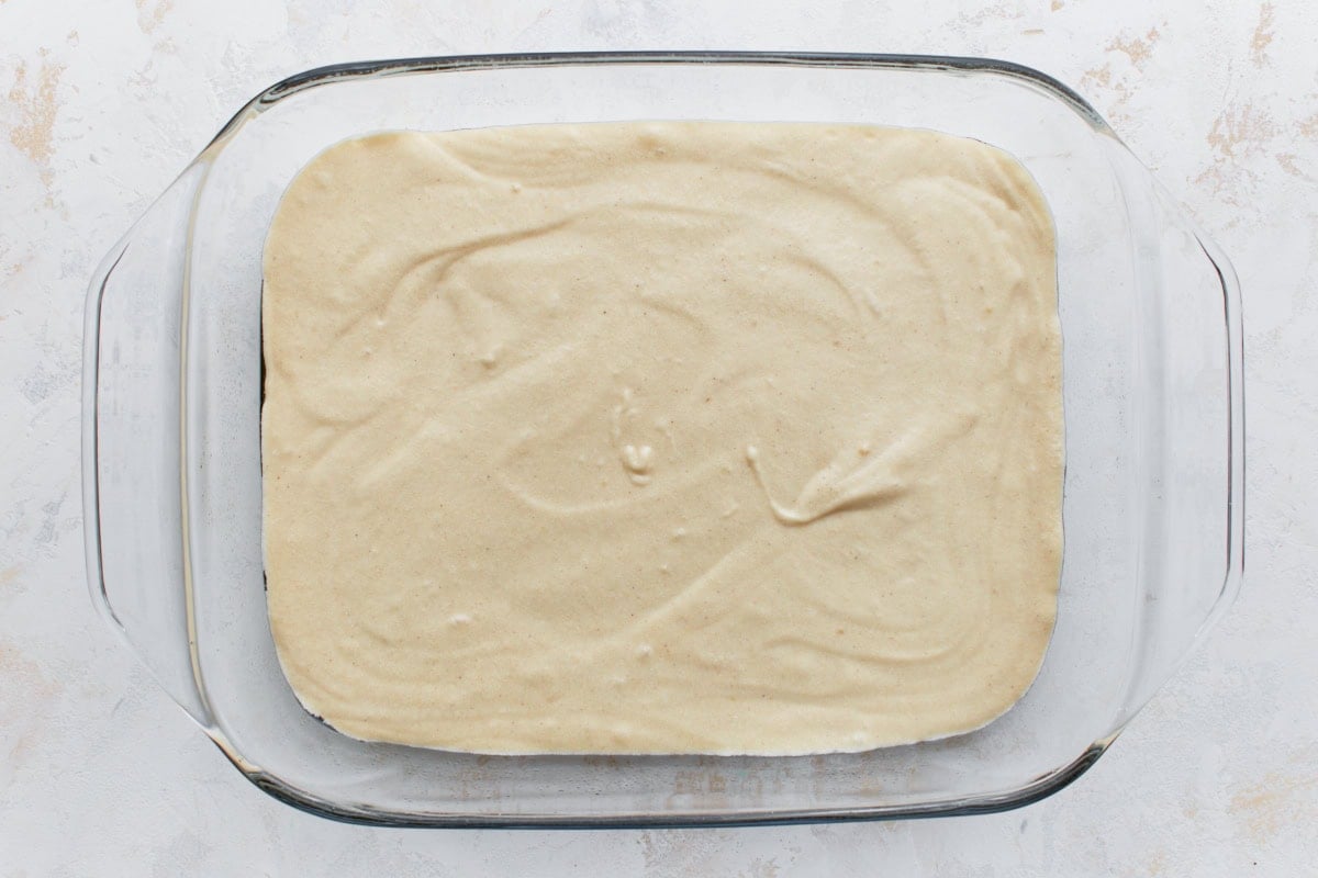 A glass baking dish filled with the first layer of gluten-free cake batter, spread evenly.