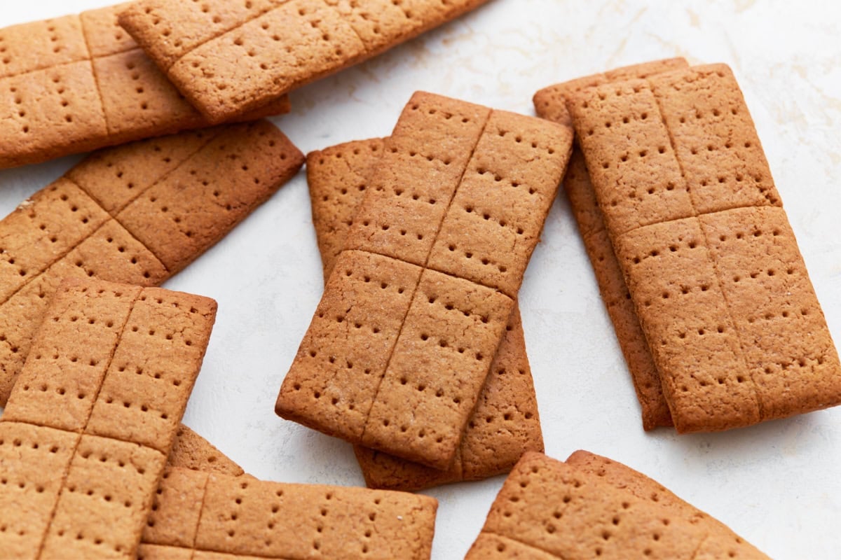 A pile of finished gluten-free graham crackers on a white surface, showing their golden-brown color and crisp texture.