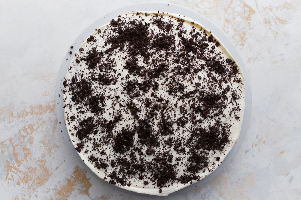 The assembled cake topped with whipped cream and a generous layer of crushed gluten-free cookies, seen from above.