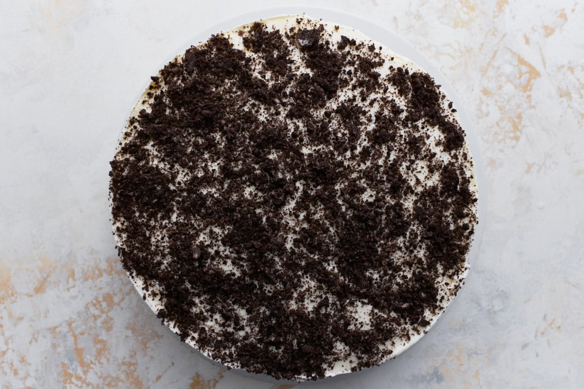 The assembled cake topped with another layer of whipped cream and a generous layer of crushed gluten-free cookies, seen from above.