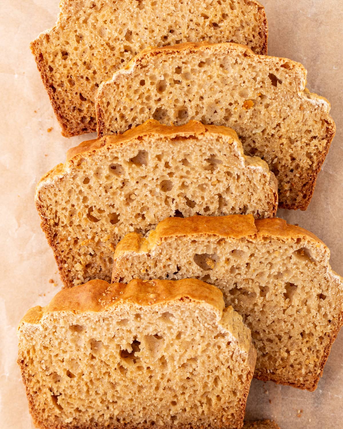 Overhead view of several slices of cassava bread arranged on parchment paper, showing a golden crust and airy crumb.