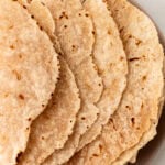 A stack of cooked cassava flour tortillas on a plate, showing lightly browned and slightly crisped edges.