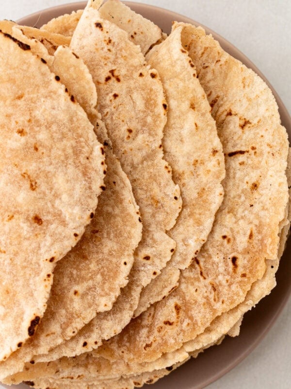 A stack of cooked cassava flour tortillas on a plate, showing lightly browned and slightly crisped edges.
