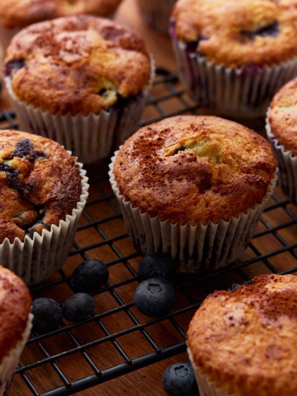 Close-up of golden-brown gluten-free blueberry muffins on a black wire cooling rack, surrounded by fresh blueberries.