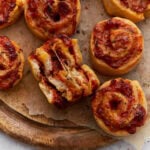 Close-up of golden-brown pizza rolls with melted cheese and tomato sauce, one roll torn open showing a gooey cheese pull.
