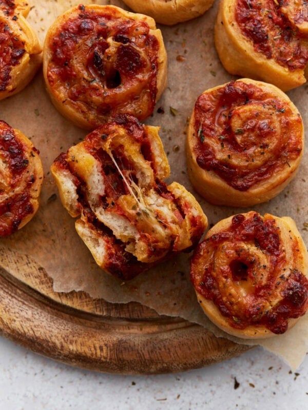 Close-up of golden-brown pizza rolls with melted cheese and tomato sauce, one roll torn open showing a gooey cheese pull.