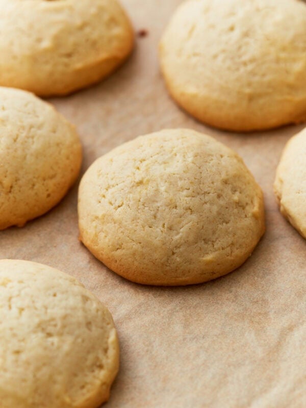 Close-up of freshly baked gluten-free vanilla wafers on parchment paper, golden brown with soft, rounded tops.