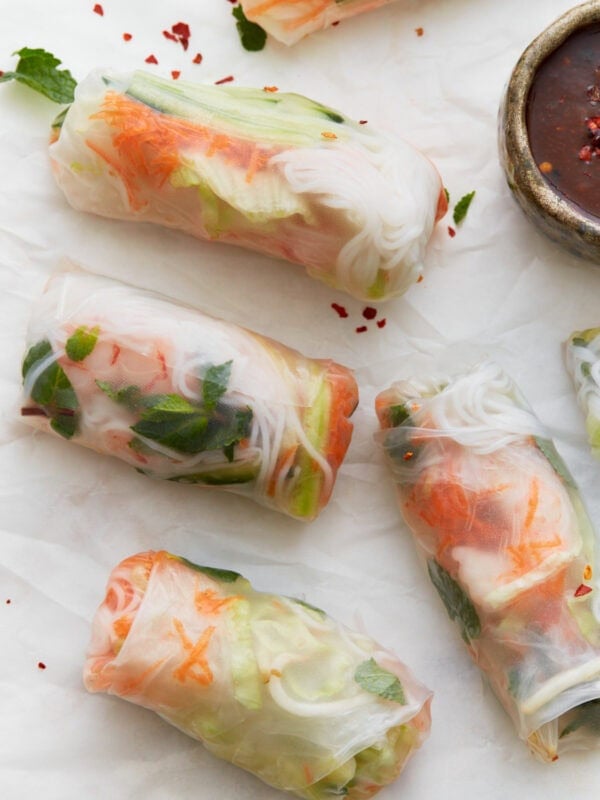 Close-up of fresh Vietnamese summer rolls filled with shrimp, vermicelli noodles, lettuce, cucumber, and herbs, served with a dark dipping sauce and garnished with chili flakes and mint.