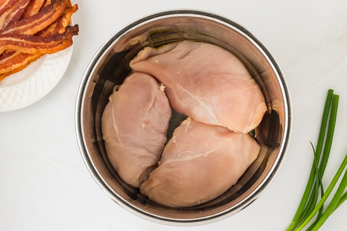 Three raw boneless chicken breasts placed in the inner pot of an Instant Pot.