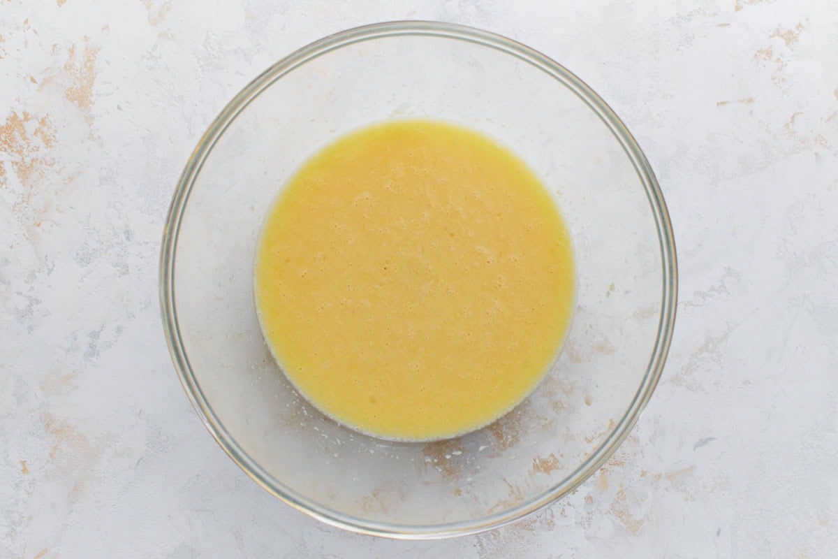 A glass bowl containing a mixture of wet ingredients, likely eggs, almond milk, and melted butter, with a smooth yellow appearance.