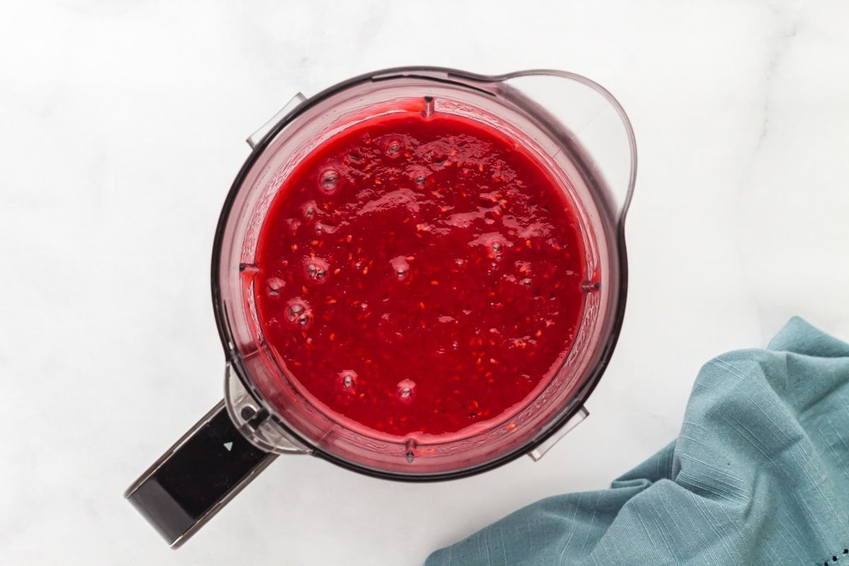 Blended raspberry mixture inside a blender pitcher, showing a smooth and vibrant red puree with a few visible seeds.