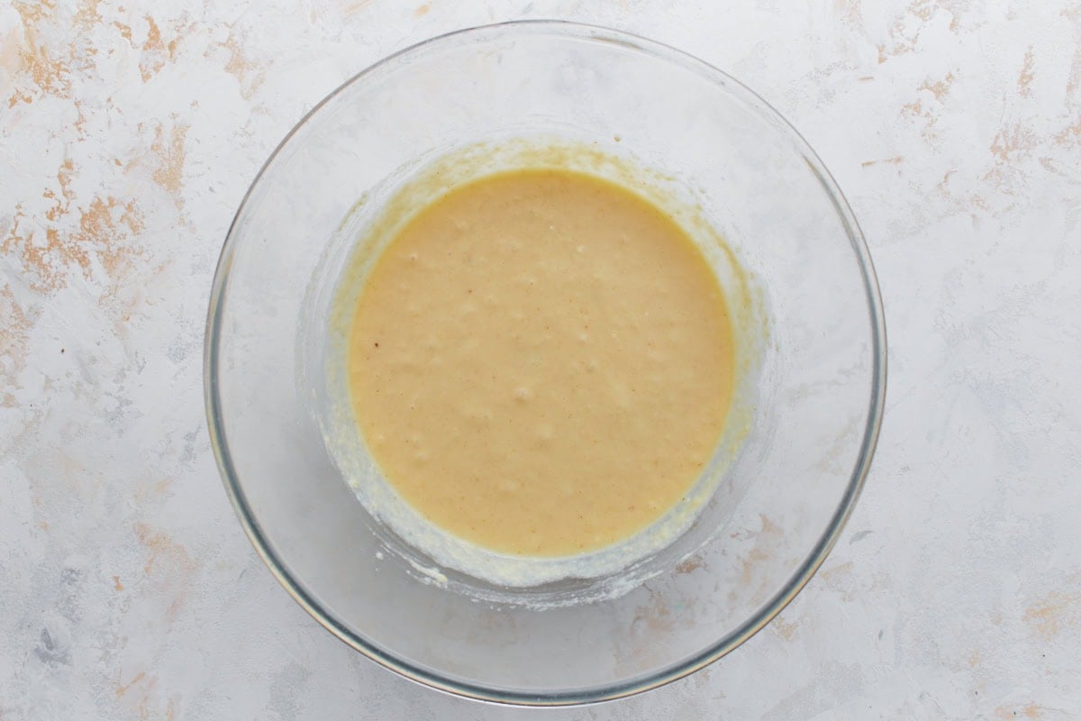 A glass bowl of fully mixed pancake batter, smooth and slightly thick with small bubbles forming.