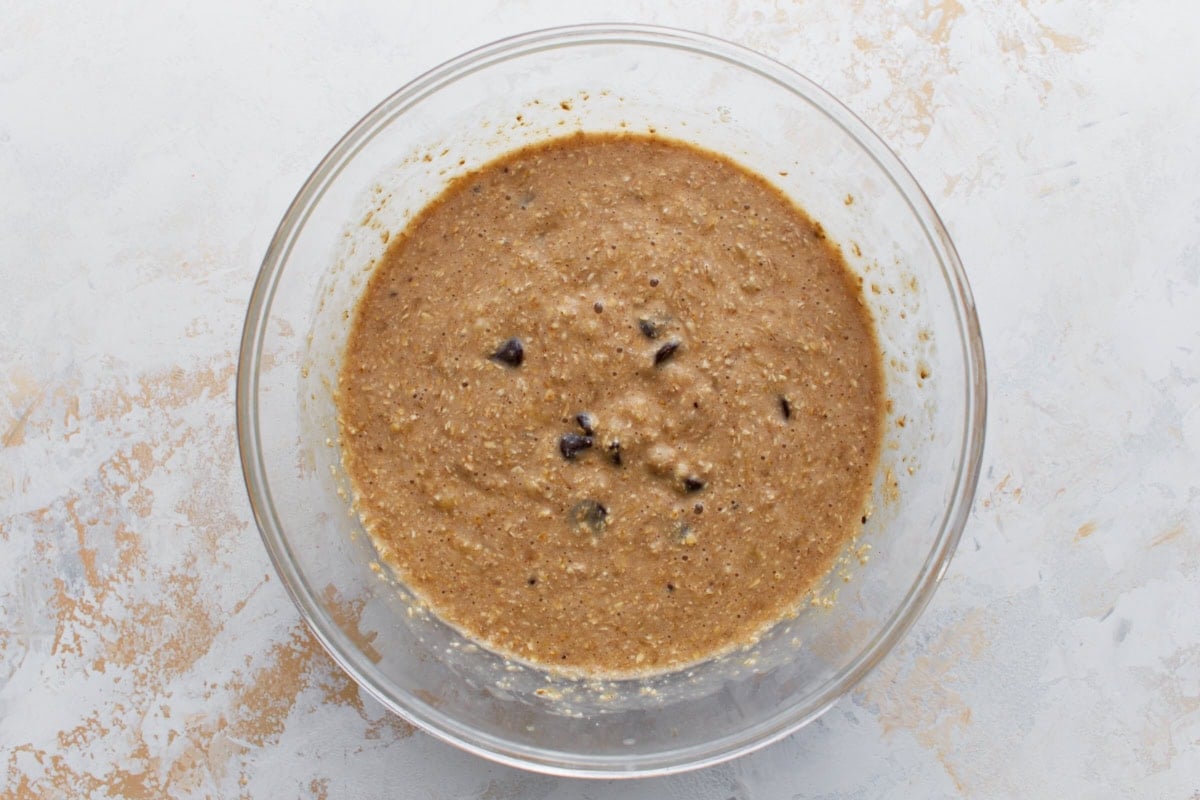 Banana bread batter in a mixing bowl with visible dark chocolate chips folded in.