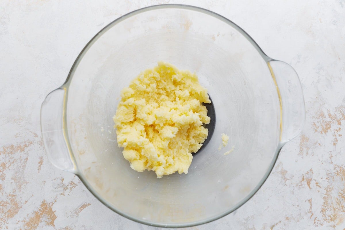 A glass mixing bowl with softened butter and granulated sugar creamed together.