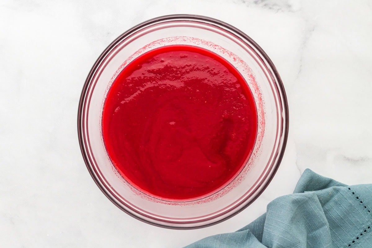 Bowl of finished raspberry coulis after straining, with a rich, silky red texture in a clear glass bowl.