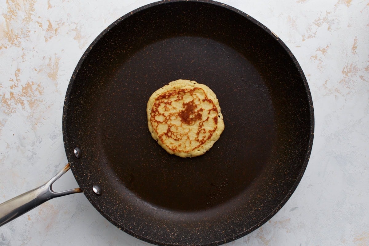 A golden-brown pancake flipped and cooking on the other side in a non-stick skillet.