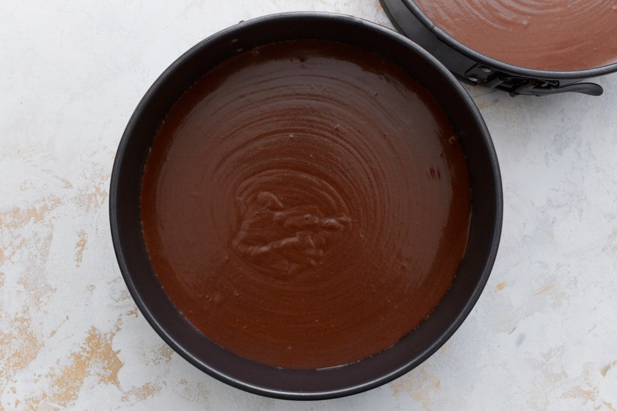Chocolate cake batter evenly spread into two prepared round pans before baking.