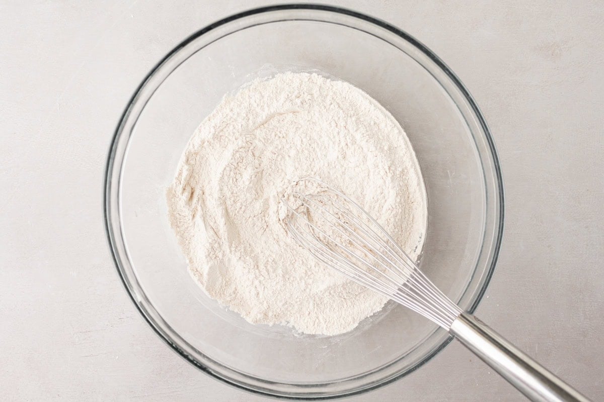 Glass bowl with a whisk resting in a pile of dry flour mixture, ready for baking cassava bread.